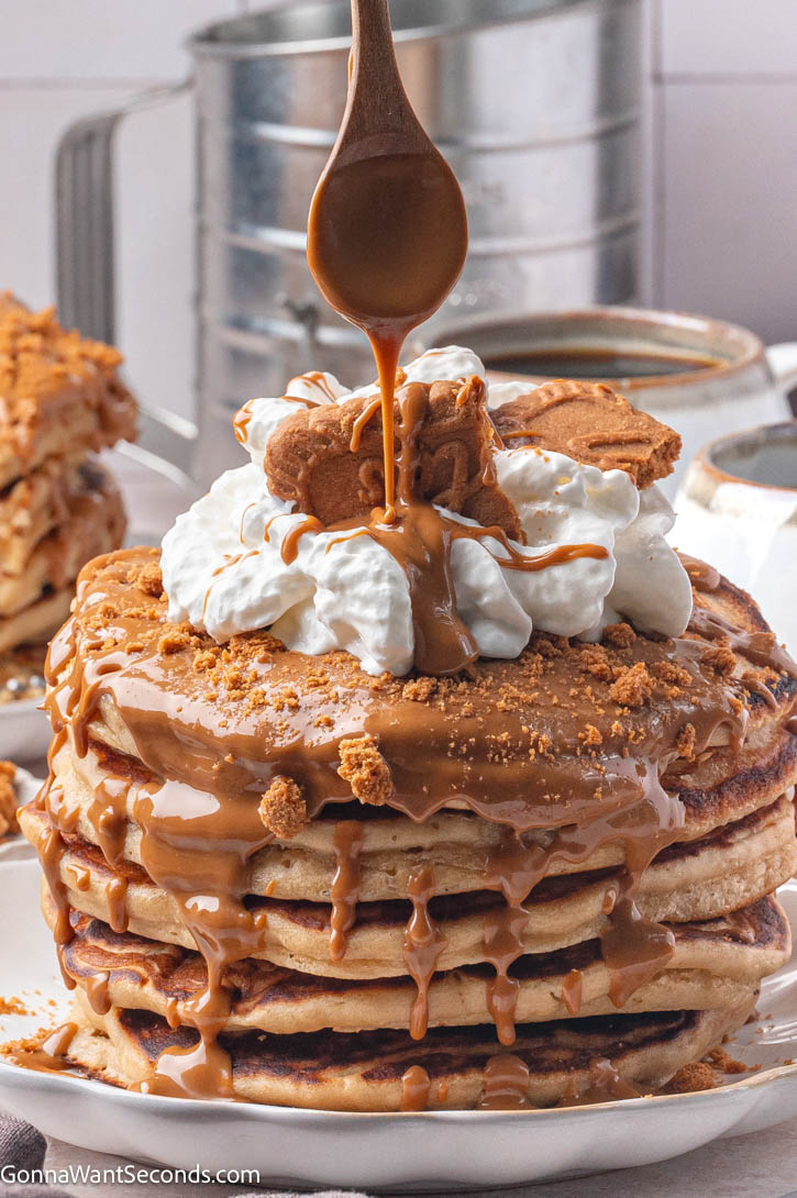 Fluffy, golden Biscoff Pancakes with cookie butter, whipped cream, and cookies — the perfect cozy breakfast treat. #pancakes #biscoffpancakes A stack of Biscoff Pancakes with cookie butter, whipped cream, on top, drizzling with warmed cookie butter