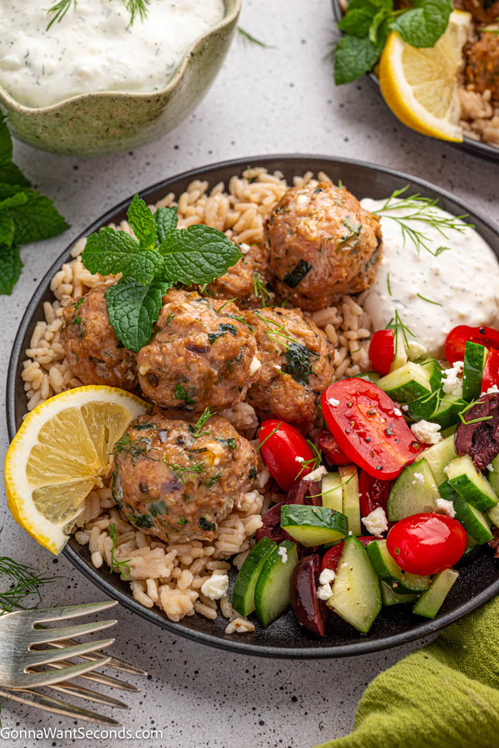 Juicy Greek turkey meatballs baked with feta, zucchini & herbs—cozy, crave-worthy comfort food your whole family will love. #turkeymeatballs #greekmeatballs Greek Turkey Meatballs on top of rice with fresh veggies and tzatziki sauce on a plate