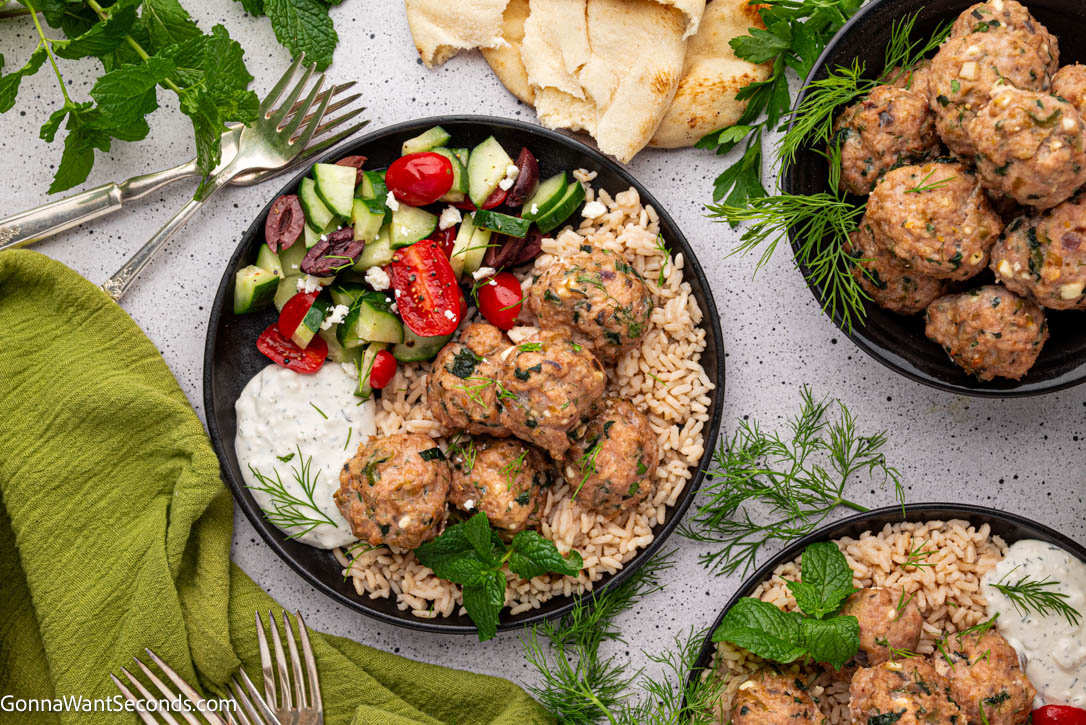 Juicy Greek turkey meatballs baked with feta, zucchini & herbs—cozy, crave-worthy comfort food your whole family will love. #turkeymeatballs #greekmeatballs Greek Turkey Meatballs on top of rice with fresh veggies and tzatziki sauce on a plate