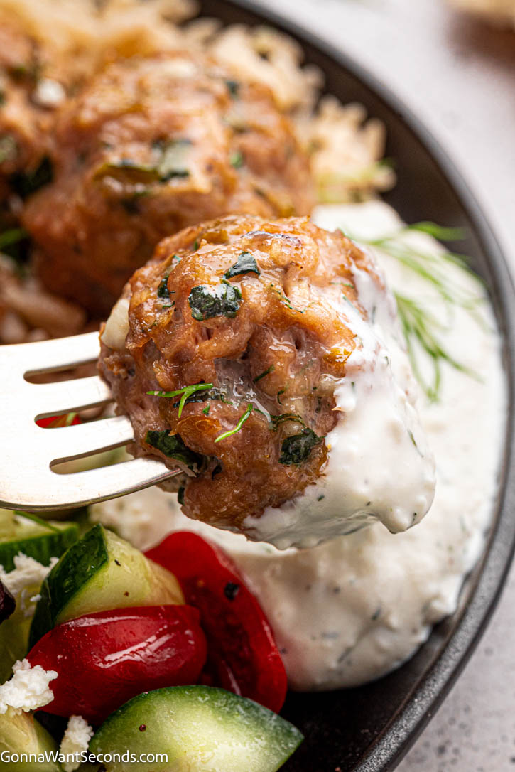 Juicy Greek turkey meatballs baked with feta, zucchini & herbs—cozy, crave-worthy comfort food your whole family will love. #turkeymeatballs #greekmeatballs Greek Turkey Meatballs on fork dipped in tzatziki sauce