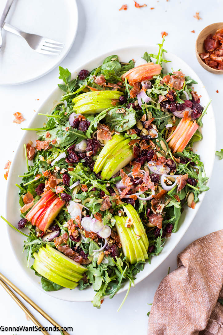 Crisp apples, goat cheese, cranberries, and prosciutto tossed in maple vinaigrette make this Harvest Salad the ultimate fall side dish. #fallsalad #harvestsalad harvest salad topped with sliced apples on an oval platter