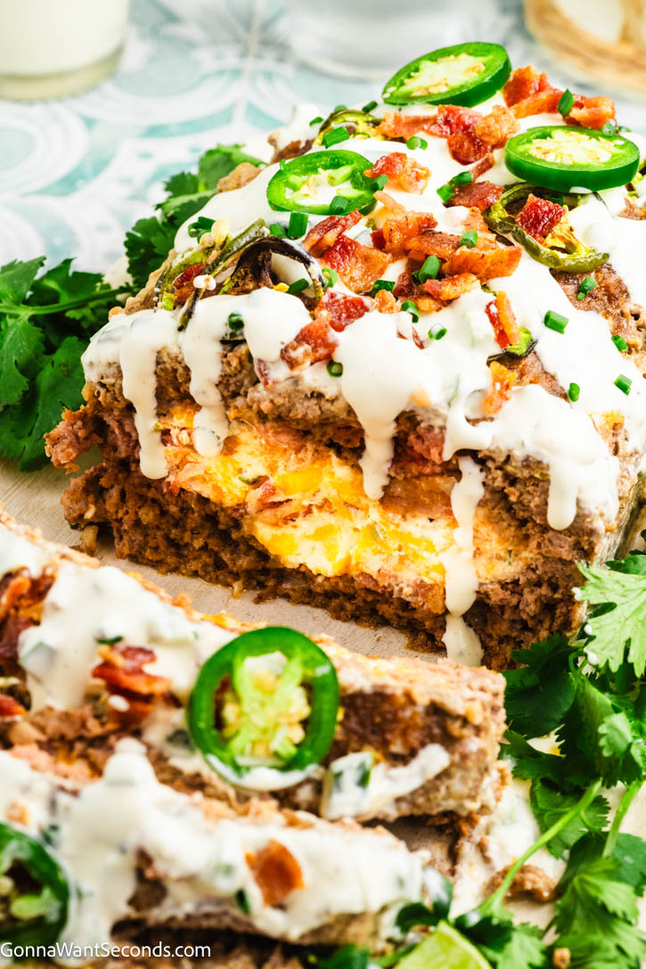 Spicy, cheesy Jalapeño Popper Meatloaf stuffed with cream cheese, cheddar, bacon, and jalapeños—comfort food made easy for family dinners. #jalapenopopper #meatloaf Jalapeño Popper Meatloaf cut in half showing the cheese filling, drizzled with creamy jalapeno sauce