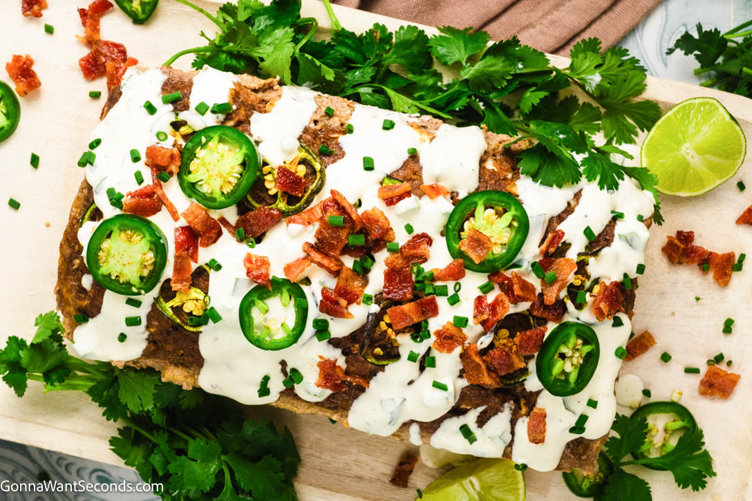 Spicy, cheesy Jalapeño Popper Meatloaf stuffed with cream cheese, cheddar, bacon, and jalapeños—comfort food made easy for family dinners. #jalapenopopper #meatloaf Whole Jalapeño Popper Meatloaf drizzled with creamy jalapeno sauce on a wooden board
