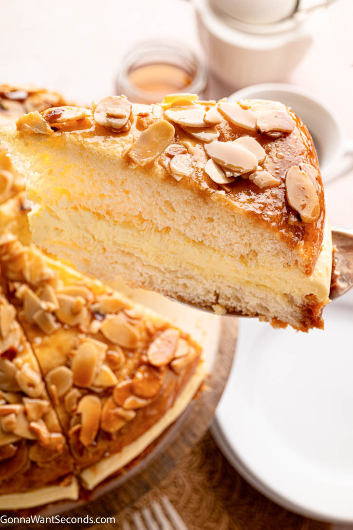 Bee Sting Cake features a soft brioche base, honey-almond topping, and creamy vanilla filling — a dreamy German dessert everyone will love! #beestingcake #bienenstich Lifting a slice German Bee Sting Cake with honey-almond topping and creamy vanilla filling