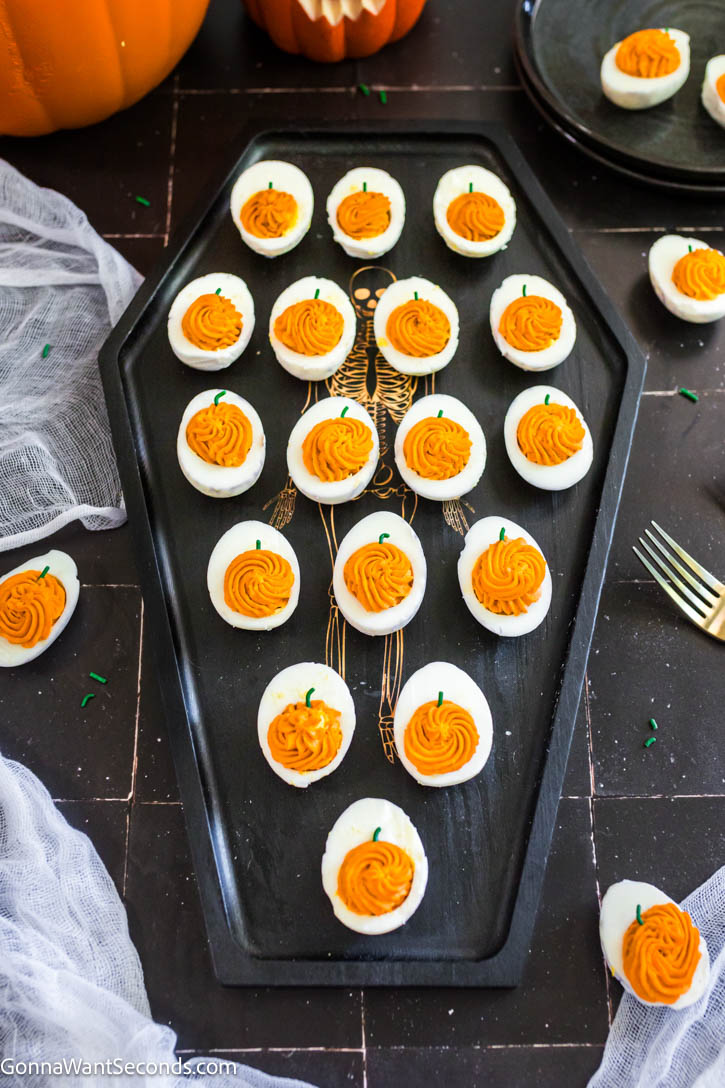These spooky-cute Halloween Deviled Eggs have black-cracked shells and creamy orange filling. It's a stunning addition to any Halloween spread! #halloweenappetizers #deviledeggs Halloween Deviled Eggs on a coffin shaped serving tray