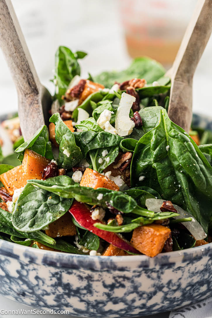 Roasted sweet potatoes, spinach, apple, feta, and pecans tossed in a maple-lemon dressing — a cozy sweet potato salad for any season! #sweetpotato #sweetpotatosalad tossing Roasted sweet potatoes with maple lemon dressing