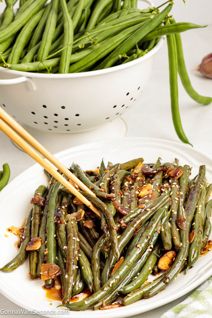 Crisp-tender Asian Green Beans tossed with garlic, ginger, and a glossy soy glaze. A quick, flavorful side ready in minutes! #greenbeans #sidedishes chopsticks picking Asian Green Beans tossed with garlic, ginger, and a glossy soy glaze