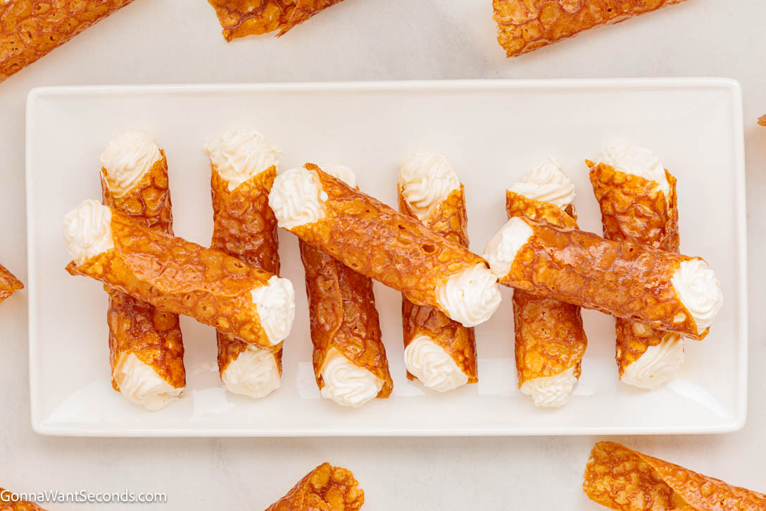 Crisp, golden, and delicately spiced, these British Brandy Snaps are buttery lace cookies filled with cream—perfect for holidays or tea time. #brandysnaps #britishbrandysnaps British Brandy Snaps with whipped cream inside on a serving dish
