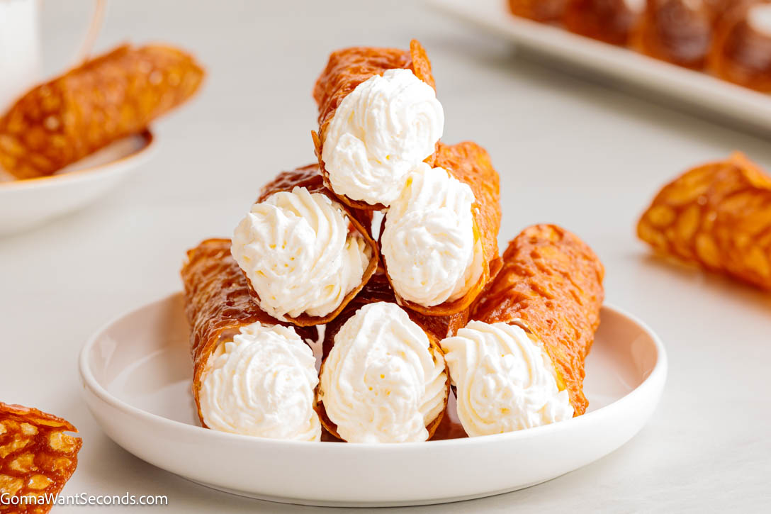 Crisp, golden, and delicately spiced, these British Brandy Snaps are buttery lace cookies filled with cream—perfect for holidays or tea time. #brandysnaps #britishbrandysnaps stacks of British Brandy Snaps with whipped cream inside