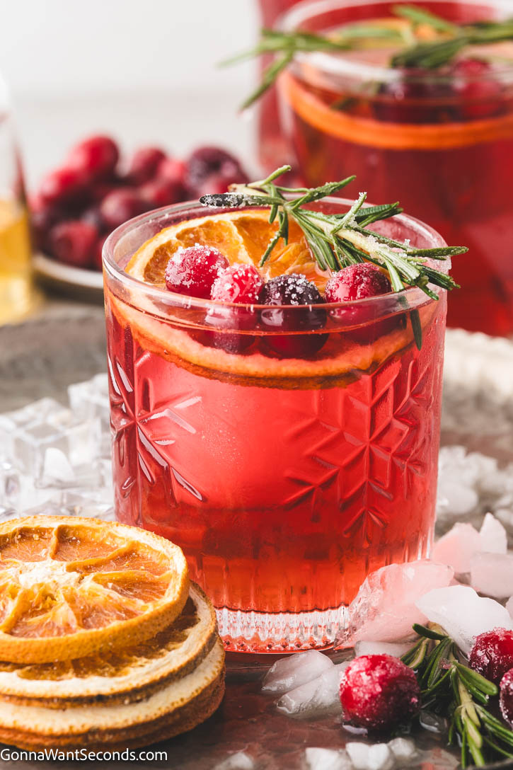 Sweet, tart, and perfectly spiced with fresh ginger and rosemary, this Christmas Cocktail will steal the show. #christmascocktail #cocktails Christmas Cocktail in a glass garnished with an orange slice, cranberries, and a rosemary spig