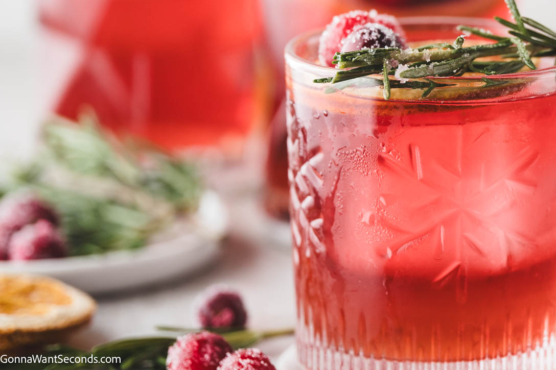 Sweet, tart, and perfectly spiced with fresh ginger and rosemary, this Christmas Cocktail will steal the show. #christmascocktail #cocktails Christmas Cocktail in a glass garnished with an orange slice, cranberries, and a rosemary spig