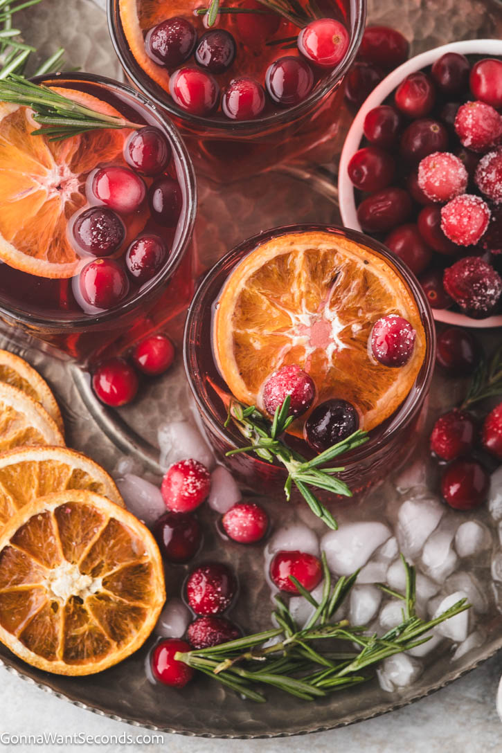 Sweet, tart, and perfectly spiced with fresh ginger and rosemary, this Christmas Cocktail will steal the show. #christmascocktail #cocktails Christmas Cocktail in a glass garnished with an orange slice, cranberries, and a rosemary spig