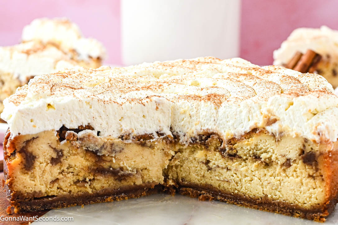 Cinnamon Roll Cheesecake has gooey cinnamon rolls, creamy cheesecake with buttery graham crust, cinnamon-swirl layers, and cream cheese frosting on top. #cinnamonroll #cinnamoncheesecake cinnamon roll cheesecake with cream cheese frosting cut in half showing layers of cinnamon-swirl layers