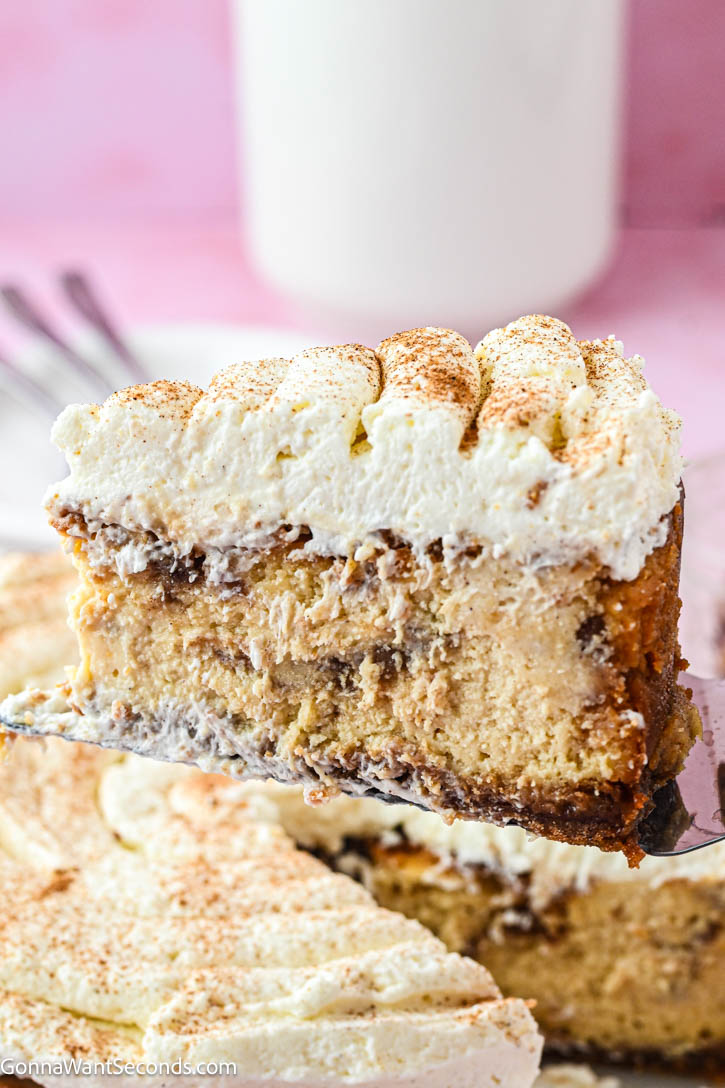 Cinnamon Roll Cheesecake has gooey cinnamon rolls, creamy cheesecake with buttery graham crust, cinnamon-swirl layers, and cream cheese frosting on top. #cinnamonroll #cinnamoncheesecake a slice of cinnamon roll cheesecake with cream cheese frosting