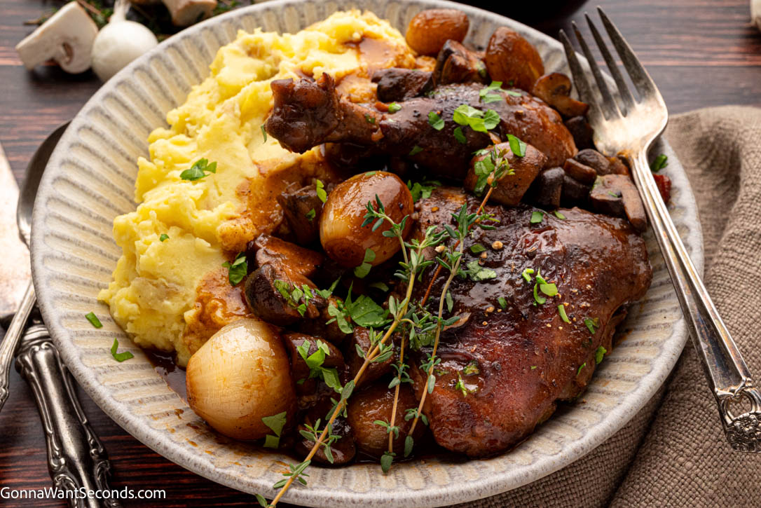 This cozy Coq Au Vin is tender chicken braised in red wine with bacon, mushrooms, and pearl onions—rich, rustic, and perfect for guests. #coqauvin #frenchchickenrecipes Coq Au Vin with mashed potato on a plate