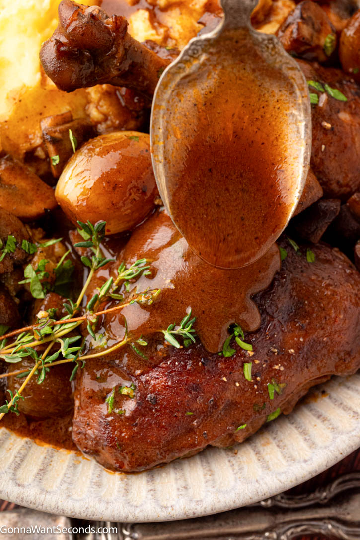 This cozy Coq Au Vin is tender chicken braised in red wine with bacon, mushrooms, and pearl onions—rich, rustic, and perfect for guests. #coqauvin #frenchchickenrecipes drizzling sauce over coq au vin