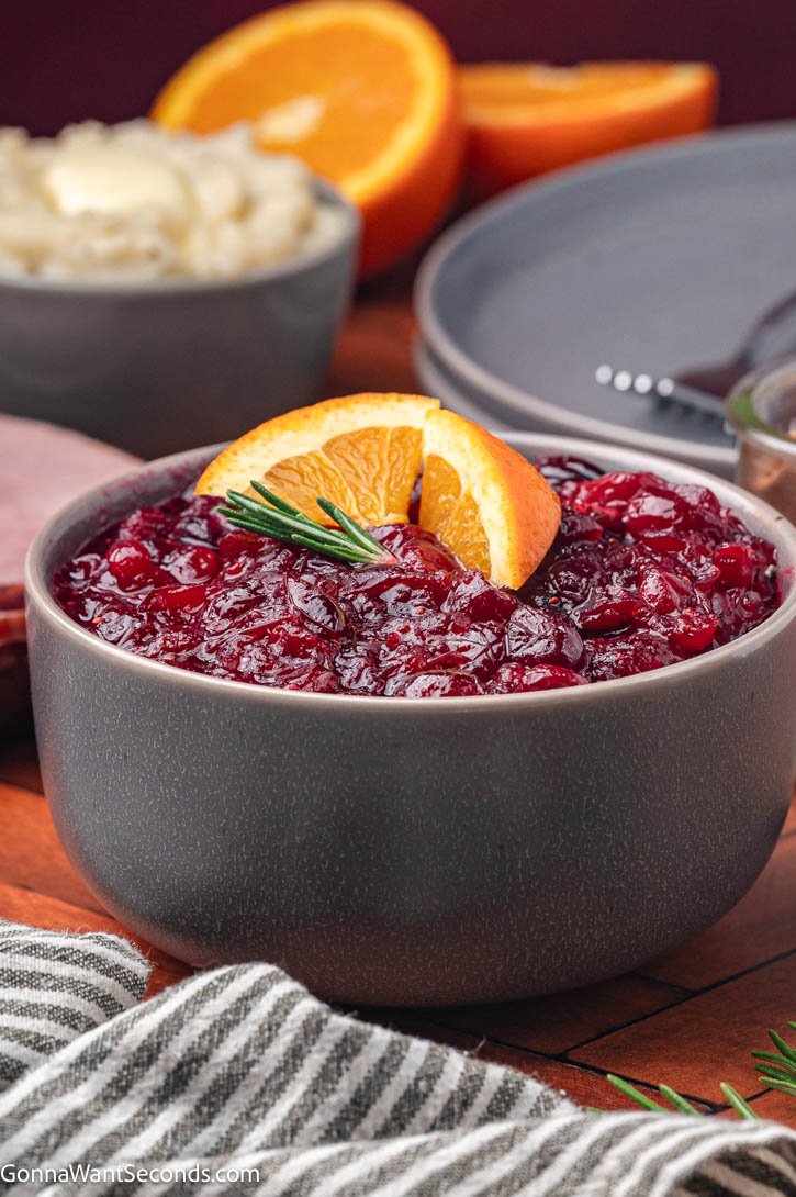 Make the best homemade cranberry sauce with fresh berries, orange juice, + cozy spices. Bright, sweet-tart + perfect for every holiday table. #cranberrysauce #cranberries homemade cranberry sauce garnished with orange slices and a sprig of rosemary on top