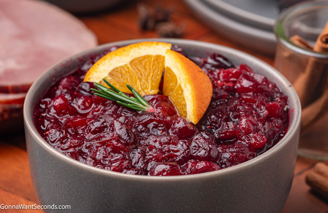 Make the best homemade cranberry sauce with fresh berries, orange juice, + cozy spices. Bright, sweet-tart + perfect for every holiday table. #cranberrysauce #cranberries homemade cranberry sauce garnished with orange slices and a sprig of rosemary on top