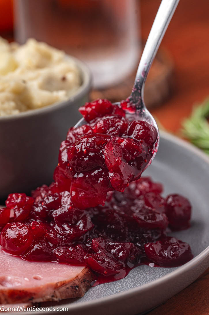 Make the best homemade cranberry sauce with fresh berries, orange juice, + cozy spices. Bright, sweet-tart + perfect for every holiday table. #cranberrysauce #cranberries pouring cranberry sauce on a slice of ham