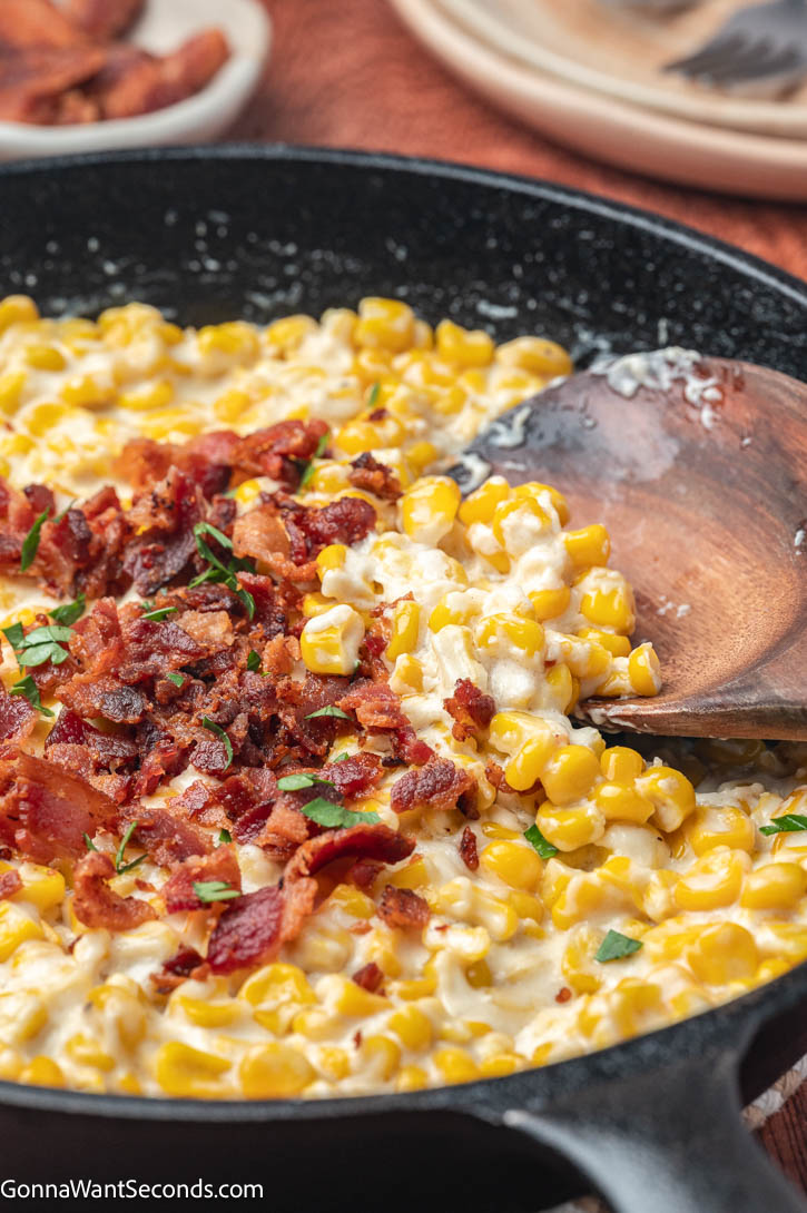 Rich, creamy, and smoky! This easy creamed corn with bacon and cream cheese is the ultimate cozy side dish for holidays or weeknight dinners. #creamedcorn creamed corn with bacon on top, on a cast iron skillet
