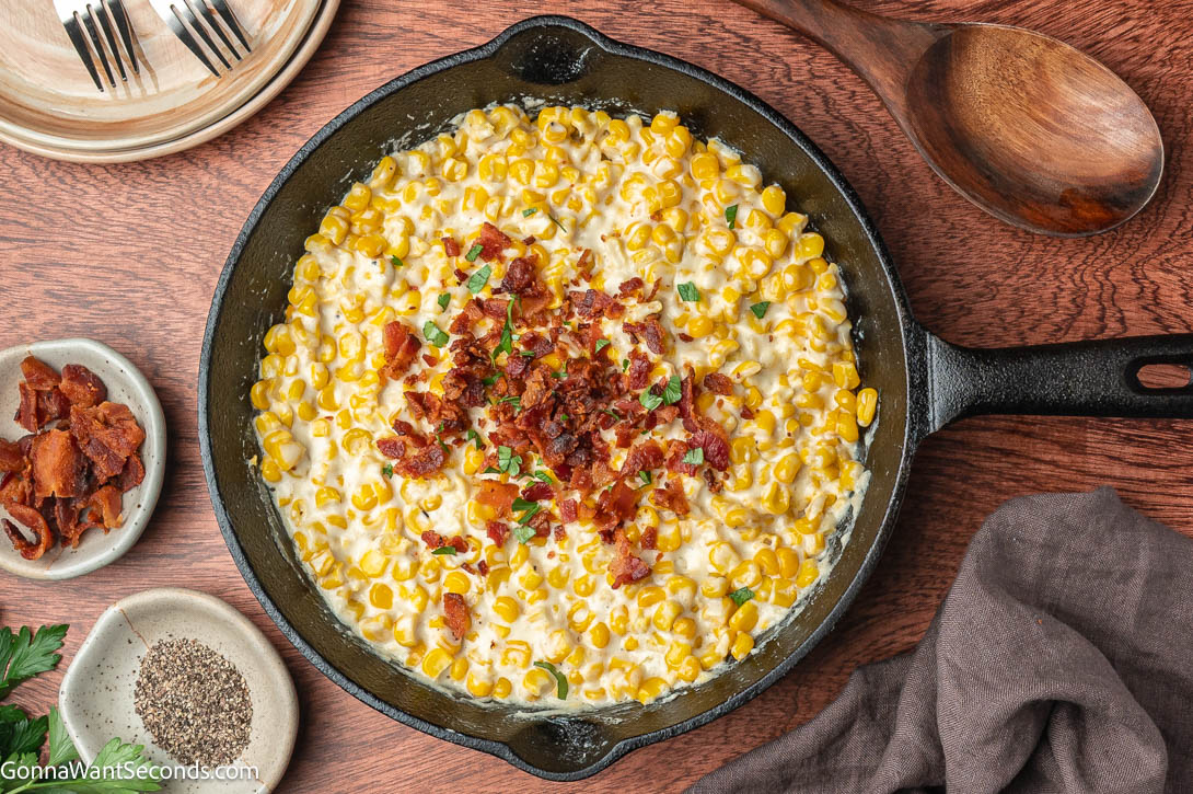 Rich, creamy, and smoky! This easy creamed corn with bacon and cream cheese is the ultimate cozy side dish for holidays or weeknight dinners. #creamedcorn creamed corn with bacon on top, on a cast iron skillet