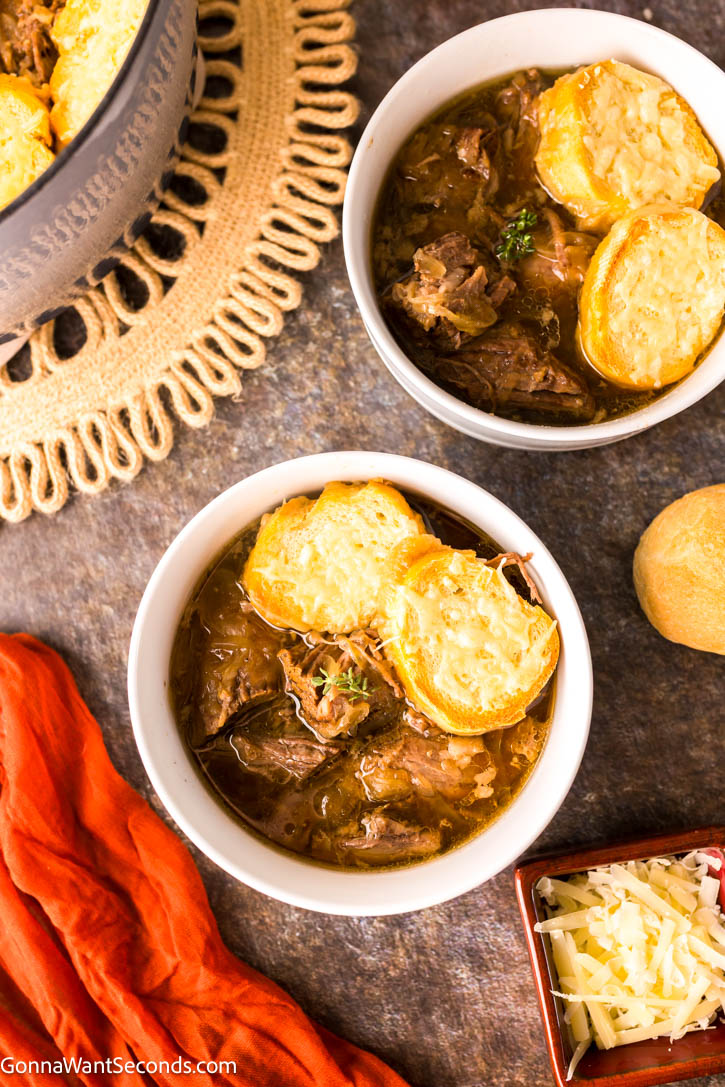 Tender beef, caramelized onions, and bubbly Gruyère make this French Onion Pot Roast a rich, comforting twist on the classic favorite. #frenchonion #potroast bowls of French Onion Pot Roast topped with baguette with melted cheese on top