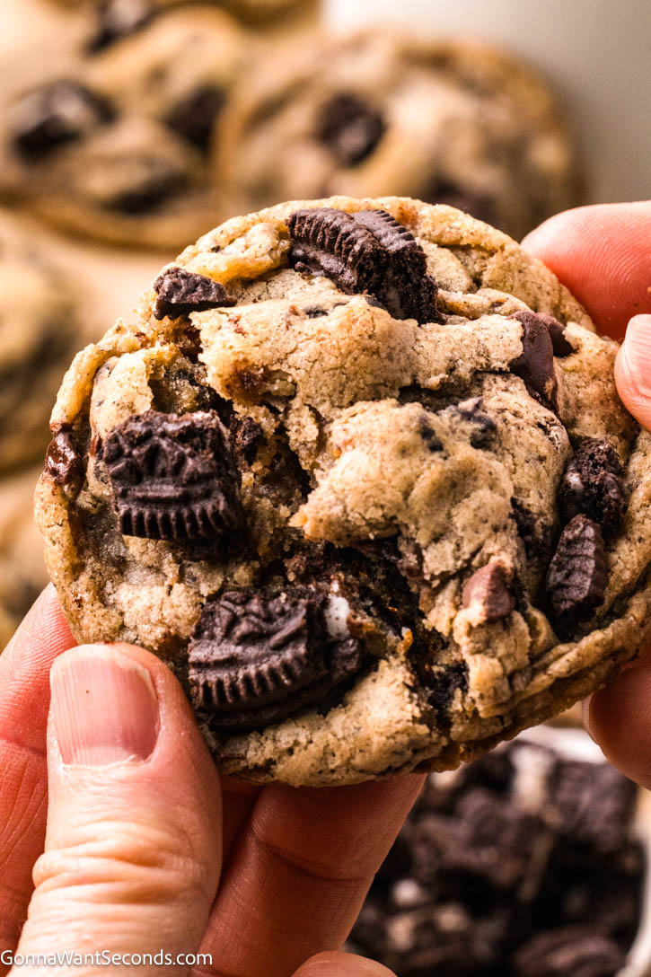 These Oreo Chocolate Chip Cookies are thick, chewy, and loaded with Oreos and brown butter flavor—the ultimate bakery-style cookie perfection! #oreocookies #chocolatechipcookies hand holding a piece of Oreo chocolate chip cookies