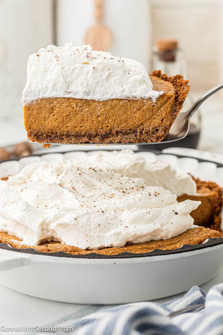 Light, airy pumpkin chiffon pie with warm spices and a buttery Biscoff crust. A dreamy make-ahead holiday dessert your family will love. #pumpkinpie #chiffonpie serving a slice of pumpkin chiffon pie with whipped topping
