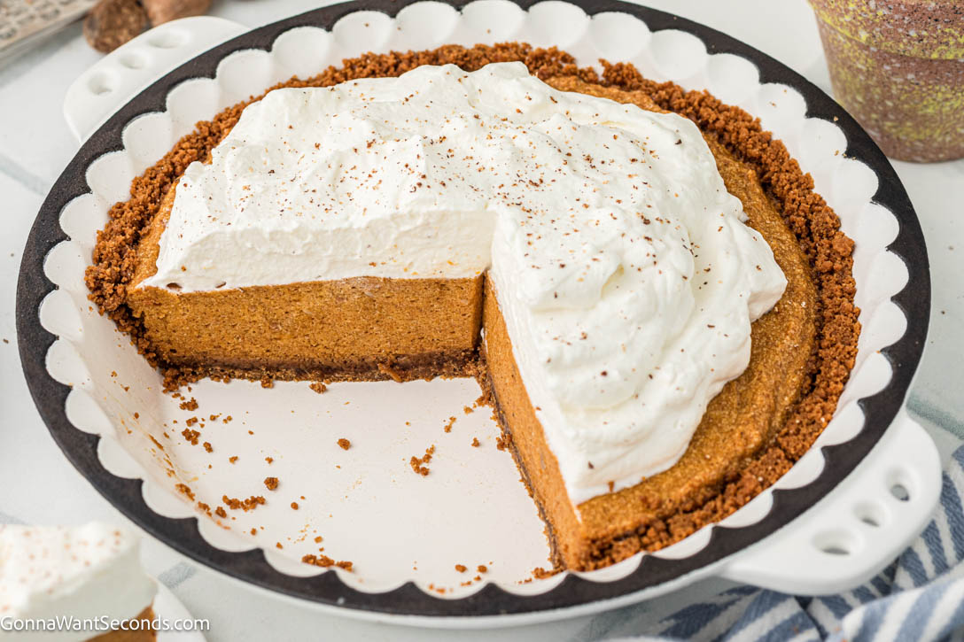 Light, airy pumpkin chiffon pie with warm spices and a buttery Biscoff crust. A dreamy make-ahead holiday dessert your family will love. #pumpkinpie #chiffonpie whole pumpkin chiffon pie with Biscoff crust and whipped topping with slices taken out