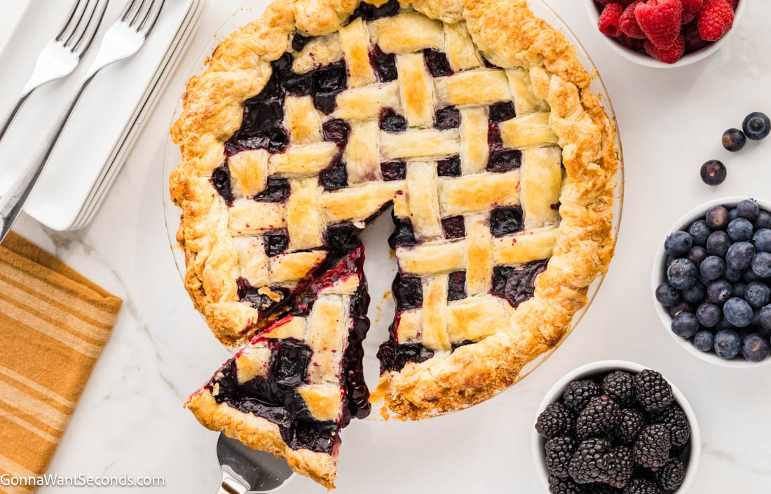 This Razzleberry Pie is made with frozen raspberries, blackberries, and blueberries, nestled inside a golden, buttery crust with a sparkling lattice top. #berrypie #razzleberrypie lifting a slice of razzleberry pie with lattice top