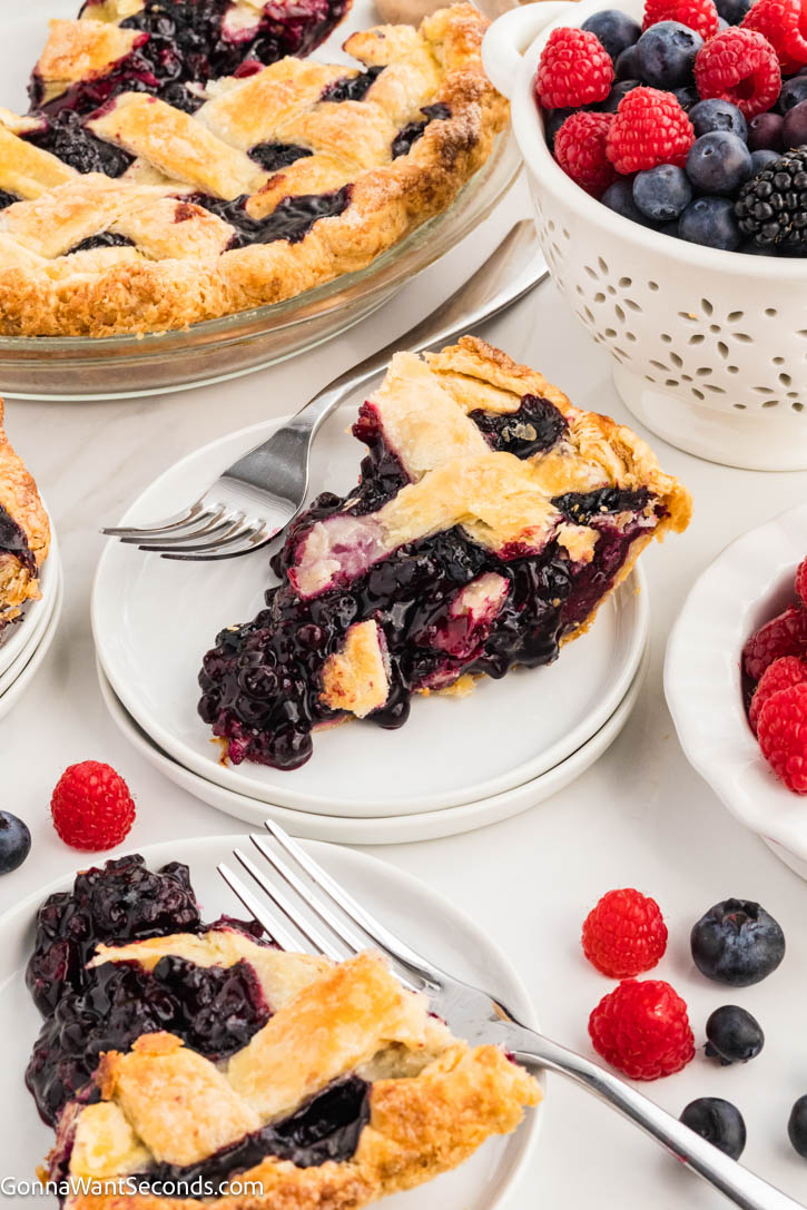 This Razzleberry Pie is made with frozen raspberries, blackberries, and blueberries, nestled inside a golden, buttery crust with a sparkling lattice top. #berrypie #razzleberrypie a slice of Razzleberry Pie with the filling spilling out on a plate