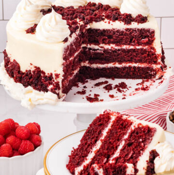 Red velvet cake topped with cream cheese frosting on a cake stand with a slice taken out on a plate