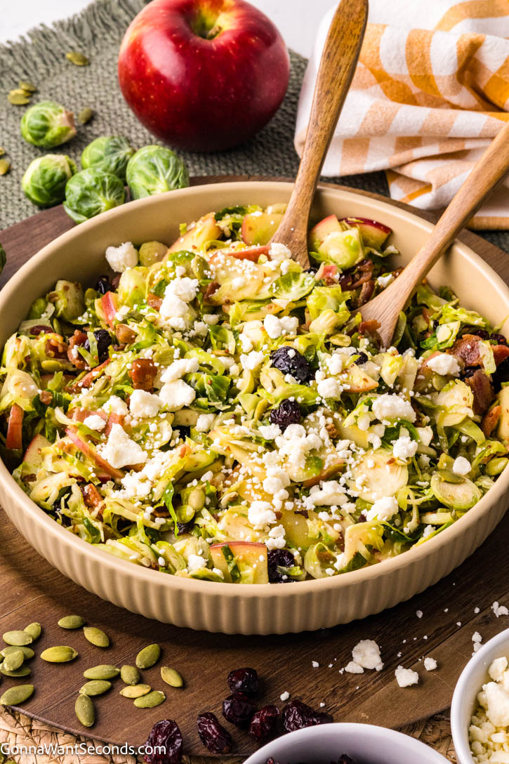 Warm shaved Brussels sprouts salad with apples, bacon, cranberries, and feta in a maple mustard dressing — cozy, colorful, and ready in 20 minutes! #Brusselssprout #Brusselssproutsalad shaved Brussels sprouts salad with apples, bacon, cranberries, and feta on a serving bowl