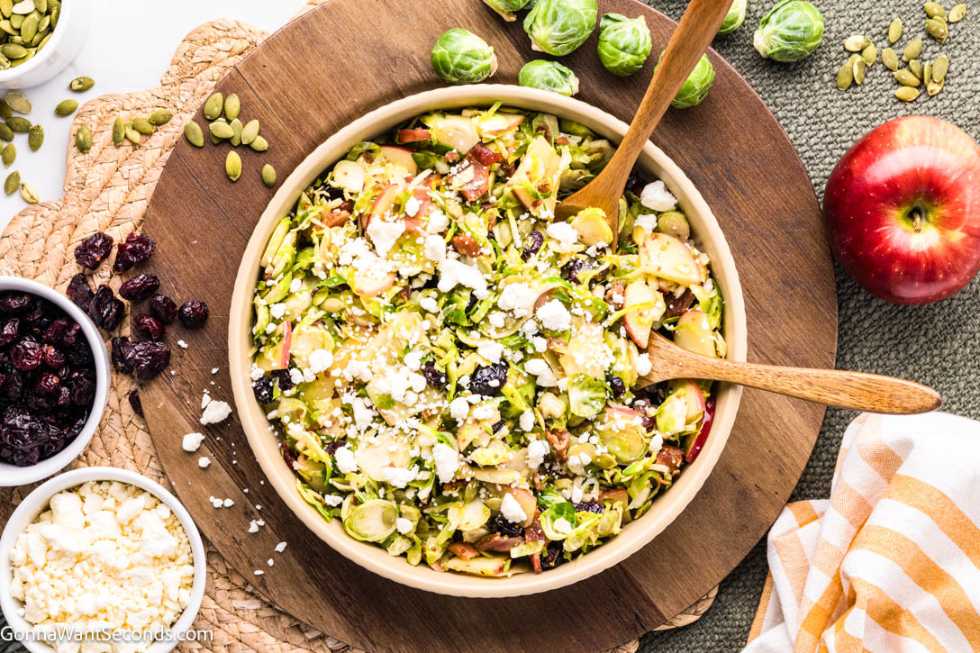 Warm shaved Brussels sprouts salad with apples, bacon, cranberries, and feta in a maple mustard dressing — cozy, colorful, and ready in 20 minutes! #Brusselssprout #Brusselssproutsalad shaved Brussels sprouts salad with apples, bacon, cranberries, and feta on a serving bowl
