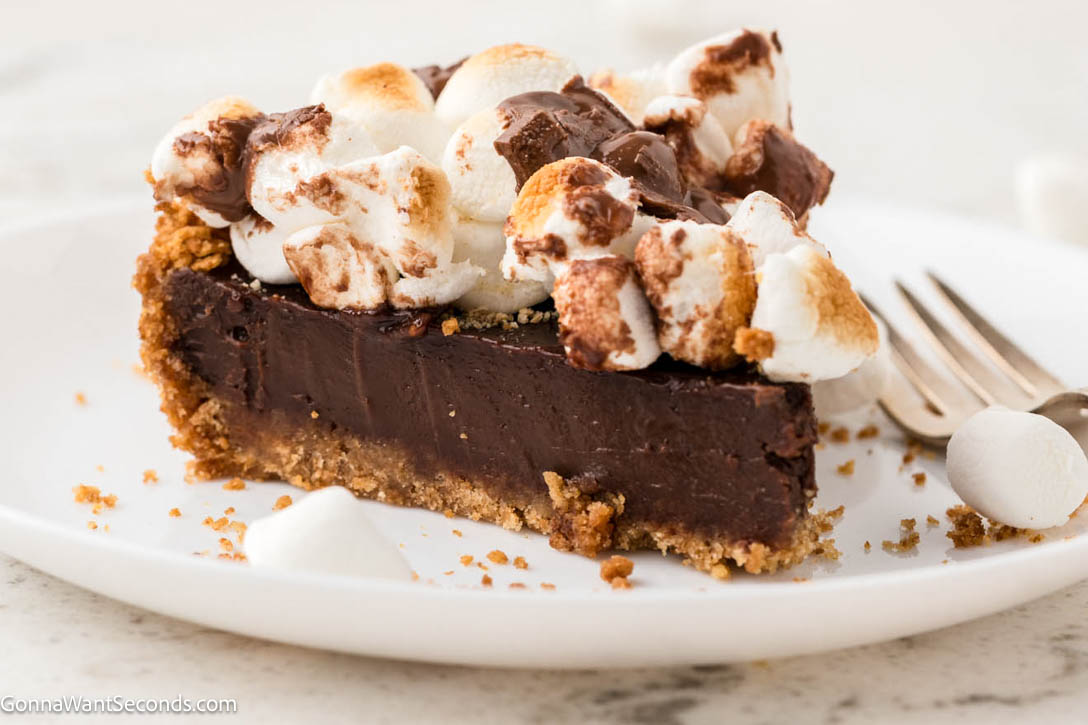 S’mores Pie has a buttery graham crust, silky chocolate filling, and golden toasted marshmallows—gooey, sliceable, and simply irresistible! #smores #smorespie a slice of smores pie showing the graham crust and chocolate filling with toasted marshmallows on top