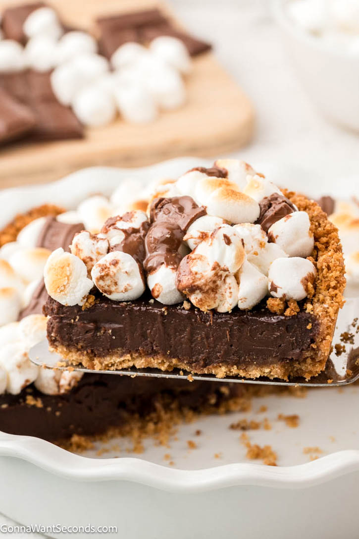 S’mores Pie has a buttery graham crust, silky chocolate filling, and golden toasted marshmallows—gooey, sliceable, and simply irresistible! #smores #smorespie lifting a slice of s'mores pie showing the graham crust and chocolate filling with toasted marshmallows on top