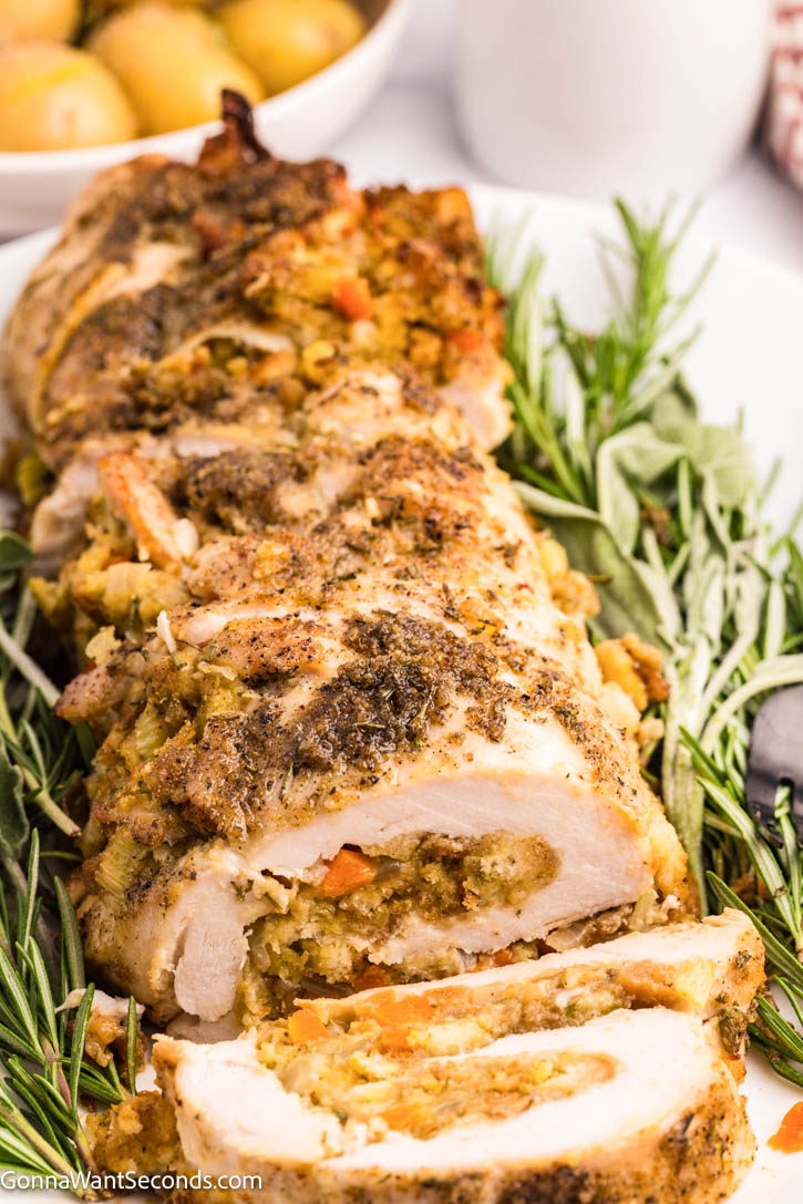 This Stuffed Turkey Breast is tender, juicy, and filled with a cozy apple-herb stuffing that tastes like the very best parts of Thanksgiving. #stuffedturkeybreast #turkeybreast Stuffed Turkey Breast with apple-herb stuffing garnished with fresh herbs on a serving platter