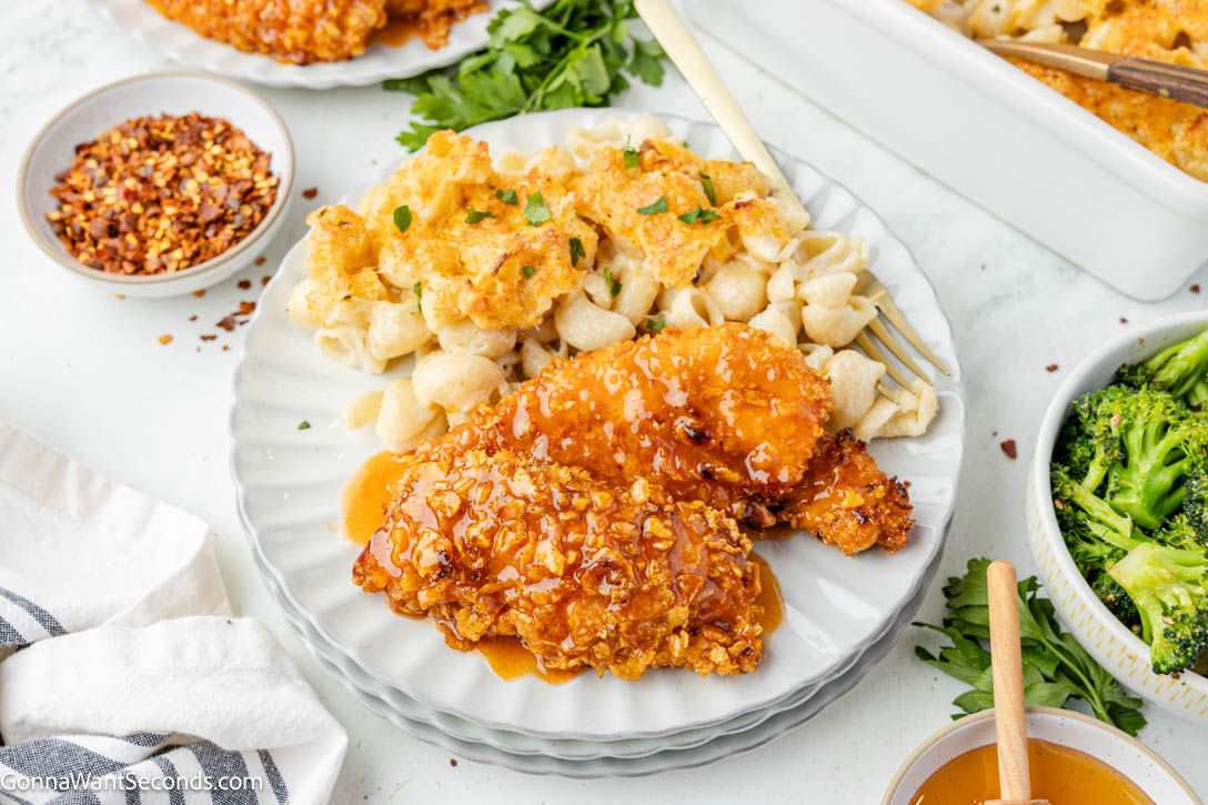 These Hot Honey Chicken Tenders are baked in the oven with a crunchy cornflake coating and finished with a sticky-sweet, lightly spicy hot honey glaze. #chickentenders #hothoneychicken hot honey crispy chicken tenders with mac and cheese on a plate