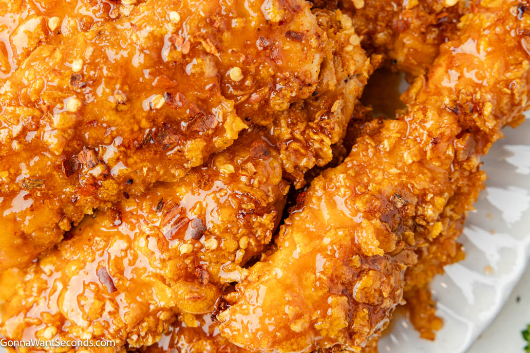 These Hot Honey Chicken Tenders are baked in the oven with a crunchy cornflake coating and finished with a sticky-sweet, lightly spicy hot honey glaze. #chickentenders #hothoneychicken Hot Honey Chicken close up