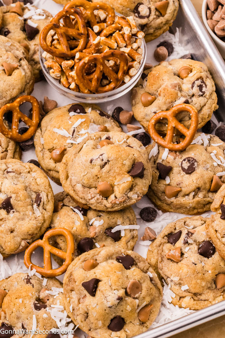 These brown butter kitchen sink cookies are thick and chewy, packed with chocolate, salted caramel, coconut, and crunchy pretzels—bakery-style too. #kitchensinkcookies #cookies Kitchen sink cookies with pretzels and chocolate morsels on a baking sheet