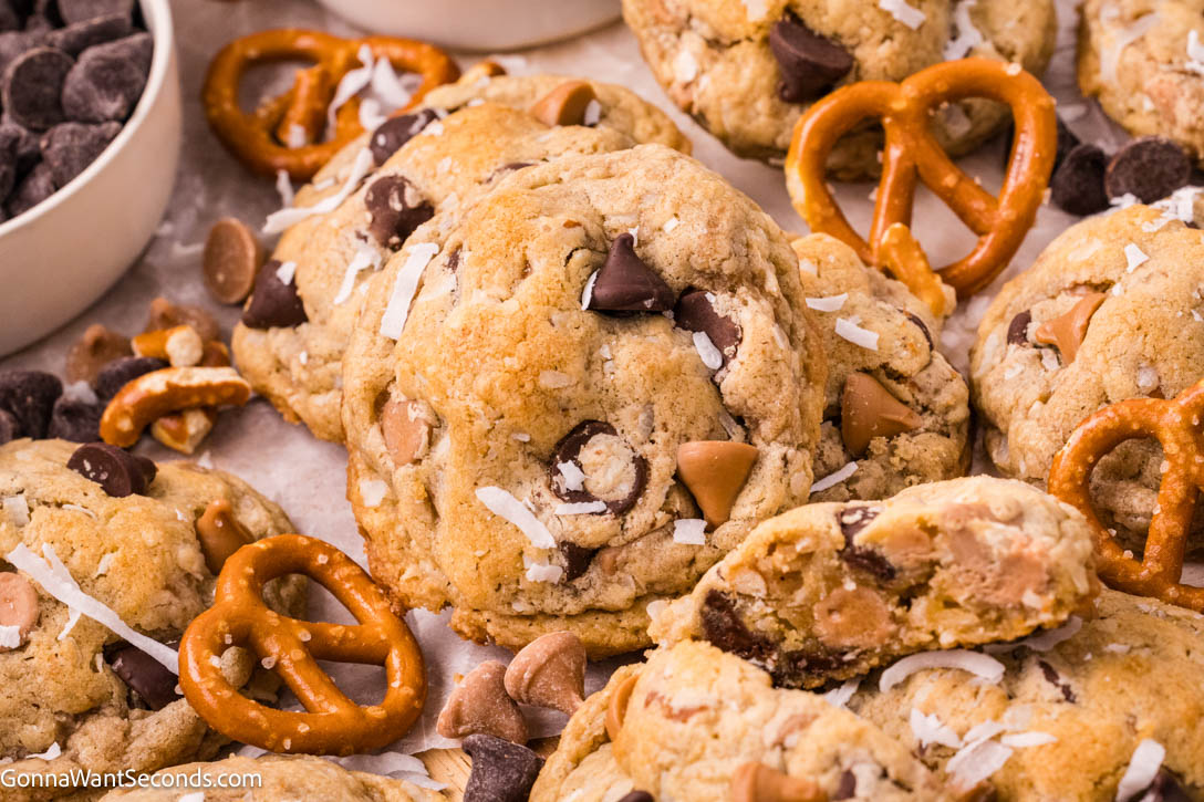 These brown butter kitchen sink cookies are thick and chewy, packed with chocolate, salted caramel, coconut, and crunchy pretzels—bakery-style too. #kitchensinkcookies #cookies Kitchen sink cookies with pretzels and chocolate morsels on a baking sheet