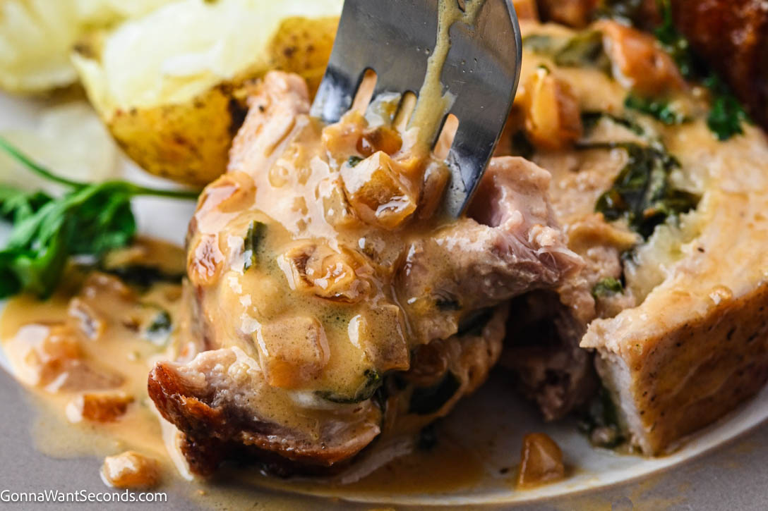 serving fork piercing stuffed pork tenderloin with spinach, gruyere with white wine cream sauce
