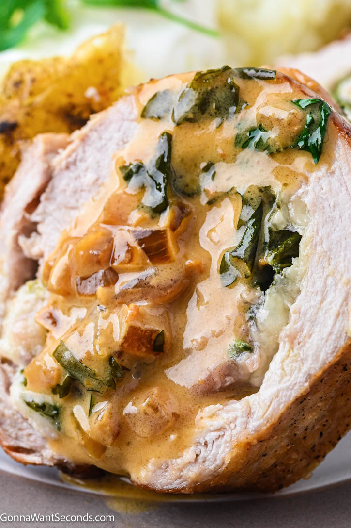 This stuffed pork tenderloin is juicy, tender, and filled with spinach + Gruyère, then finished with a silky white wine cream sauce. #stuffedpork #porktenderloin a slice of stuffed pork tenderloin with spinach, gruyere with white wine cream sauce