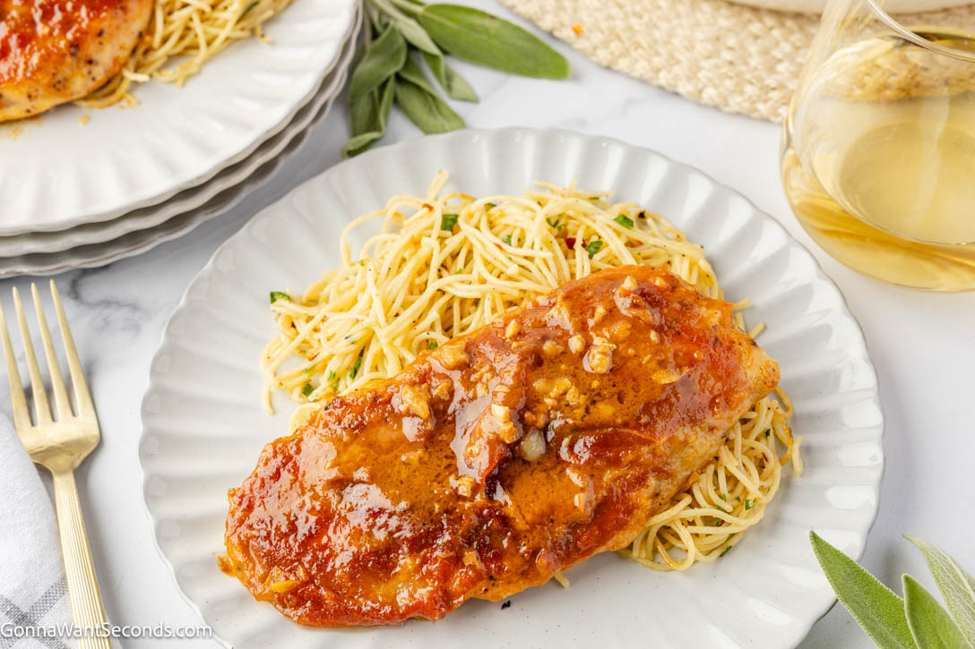 Chicken Saltimbocca is a fancy but easy, 30-minute pan-seared chicken cutlet, elegantly topped with sage and prosciutto, with white wine butter sauce. #chickensaltimbocca #30minutemeals a piece of Chicken Saltimbocca coated with sauce on top of pasta on a plate