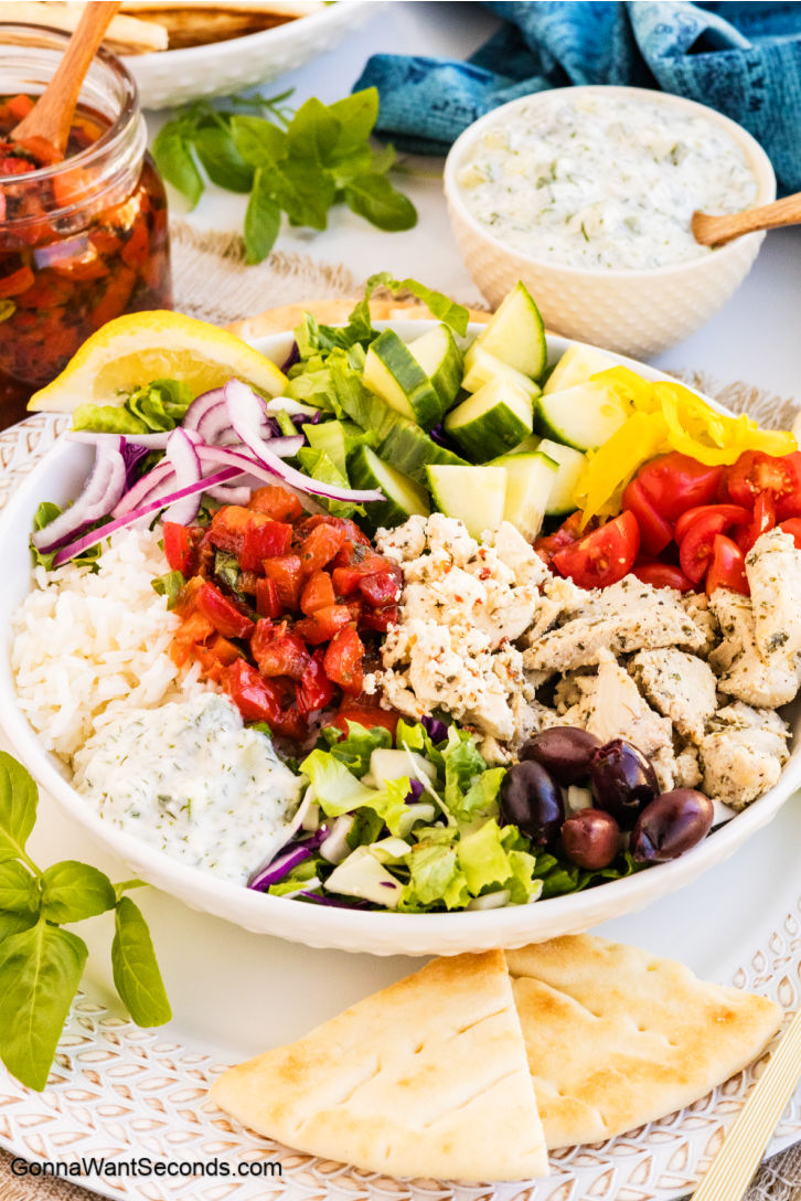 Greek Chicken Bowls are made with yogurt-marinated chicken, roasted red peppers, feta, olives, crisp veggies, and vinaigrette. It's fresh, flexible, and easy! #greekchicken #greekchickenbowls Greek Chicken Bowls with chicken, rice, and vegetables in a bowl