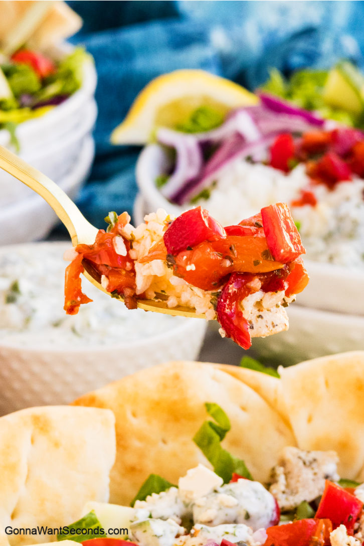 Greek Chicken Bowls are made with yogurt-marinated chicken, roasted red peppers, feta, olives, crisp veggies, and vinaigrette. It's fresh, flexible, and easy! #greekchicken #greekchickenbowls A fork-filled Greek Chicken Bowls