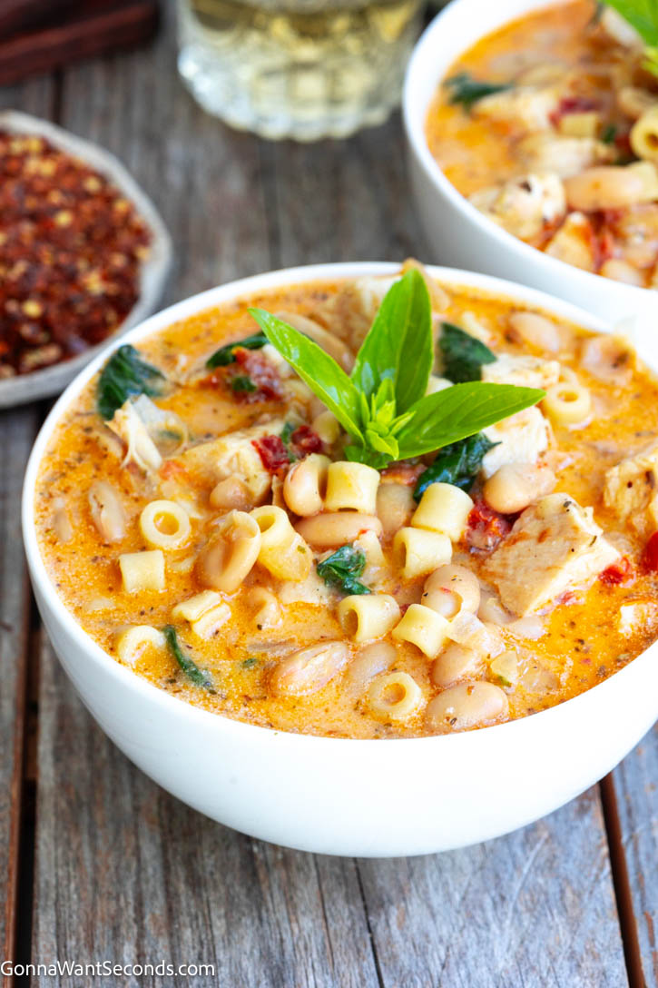 Creamy Tuscan chicken soup with juicy chicken breast, ditalini, sun-dried tomatoes, spinach, and Parmesan—cozy one-pot comfort for busy weeknights. #tuscanchickensoup #chickensoup Creamy Tuscan chicken soup with spinach garnished with fresh basil on a bowl