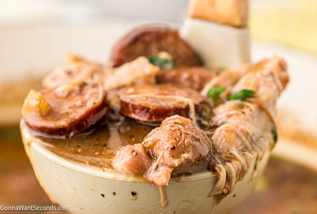 Authentic Cajun chicken and sausage gumbo with a deep dark roux, smoky andouille, and bold flavor. Tomato-free and rich. #chickengumbo #gumbo Ladle scooping Cajun chicken and sausage gumbo