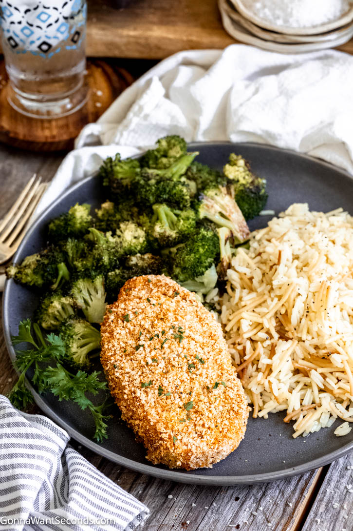 These shake and bake pork chops bake up golden and crisp on the outside while staying tender and juicy inside. #bakedporkchops #porkchops shake and bake pork chops with rice pilaf and roasted broccoli on a plate