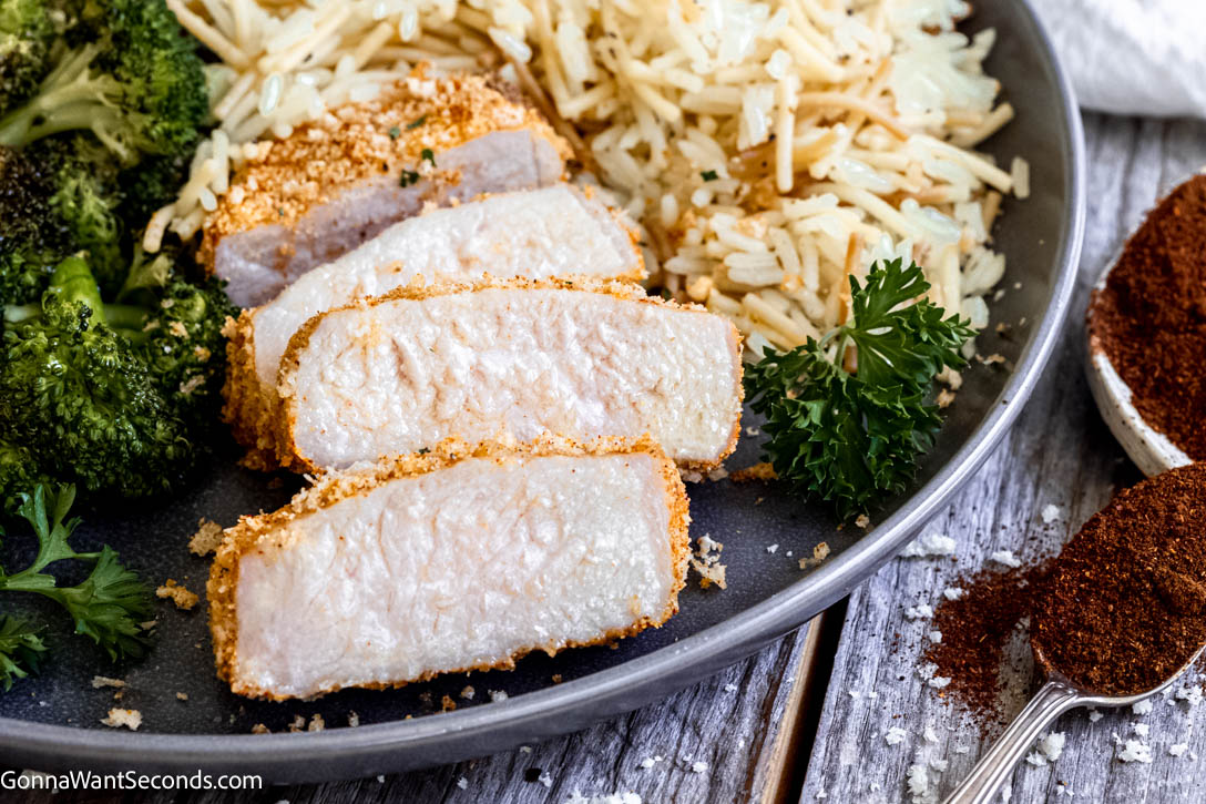 These shake and bake pork chops bake up golden and crisp on the outside while staying tender and juicy inside. #bakedporkchops #porkchops sliced shake and bake pork chops with rice pilaf and roasted broccoli on a plate